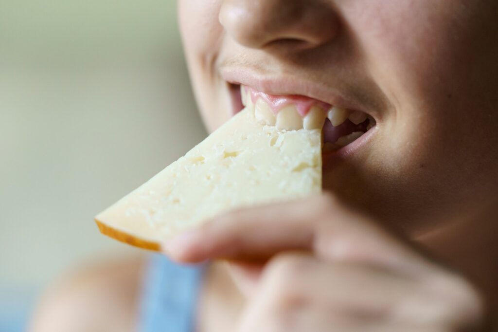 Crop happy unrecognizable girl biting fresh cheese slice