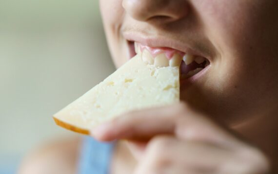 Crop happy unrecognizable girl biting fresh cheese slice